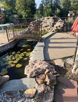 Pond with a small bridge, lined with rocks. Water lilies float in the water.