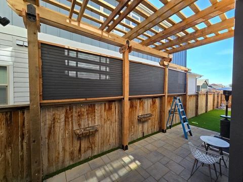 Arborist in harness cutting a tall tree under a blue sky, residential setting.