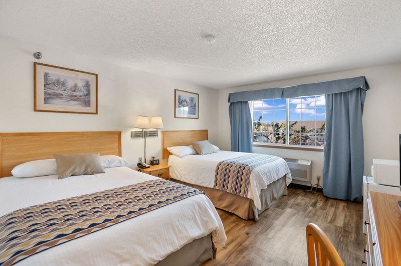 A hotel room with two beds, closet, mini fridge, coffee maker, and a window.