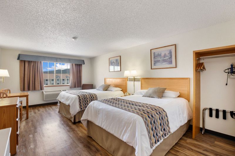 A hotel room with two beds , a desk , closet, mini fridge, coffee maker, and a window.