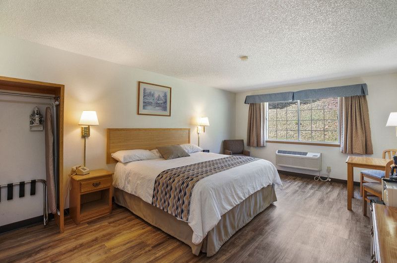 A hotel room with a king size bed , desk,  closet, mini fridge, coffee maker,  window.