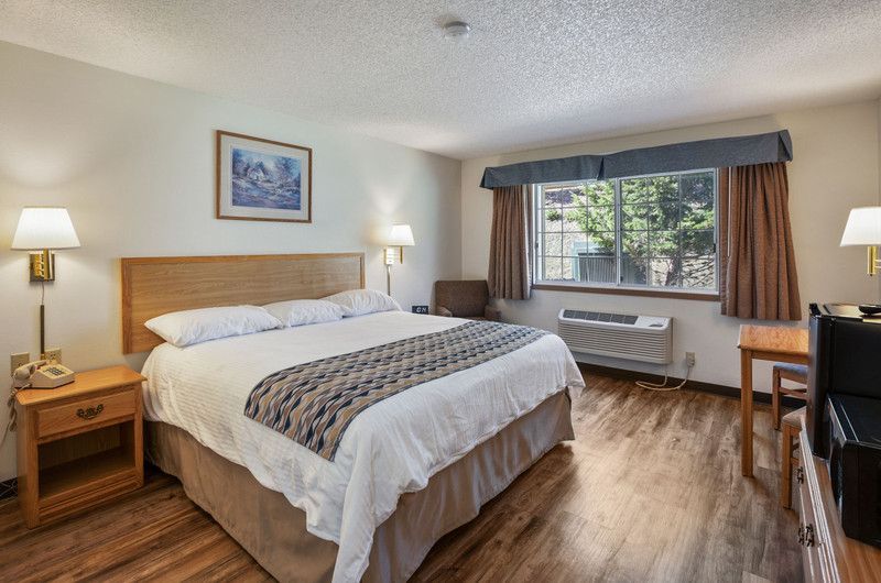 A hotel room with a king size bed closet, mini fridge, coffee maker,  a large window.