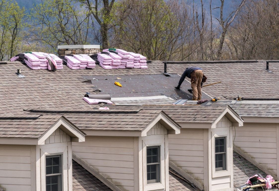 Roofer working on a residential roof, stacks of pink insulation and shingles nearby.