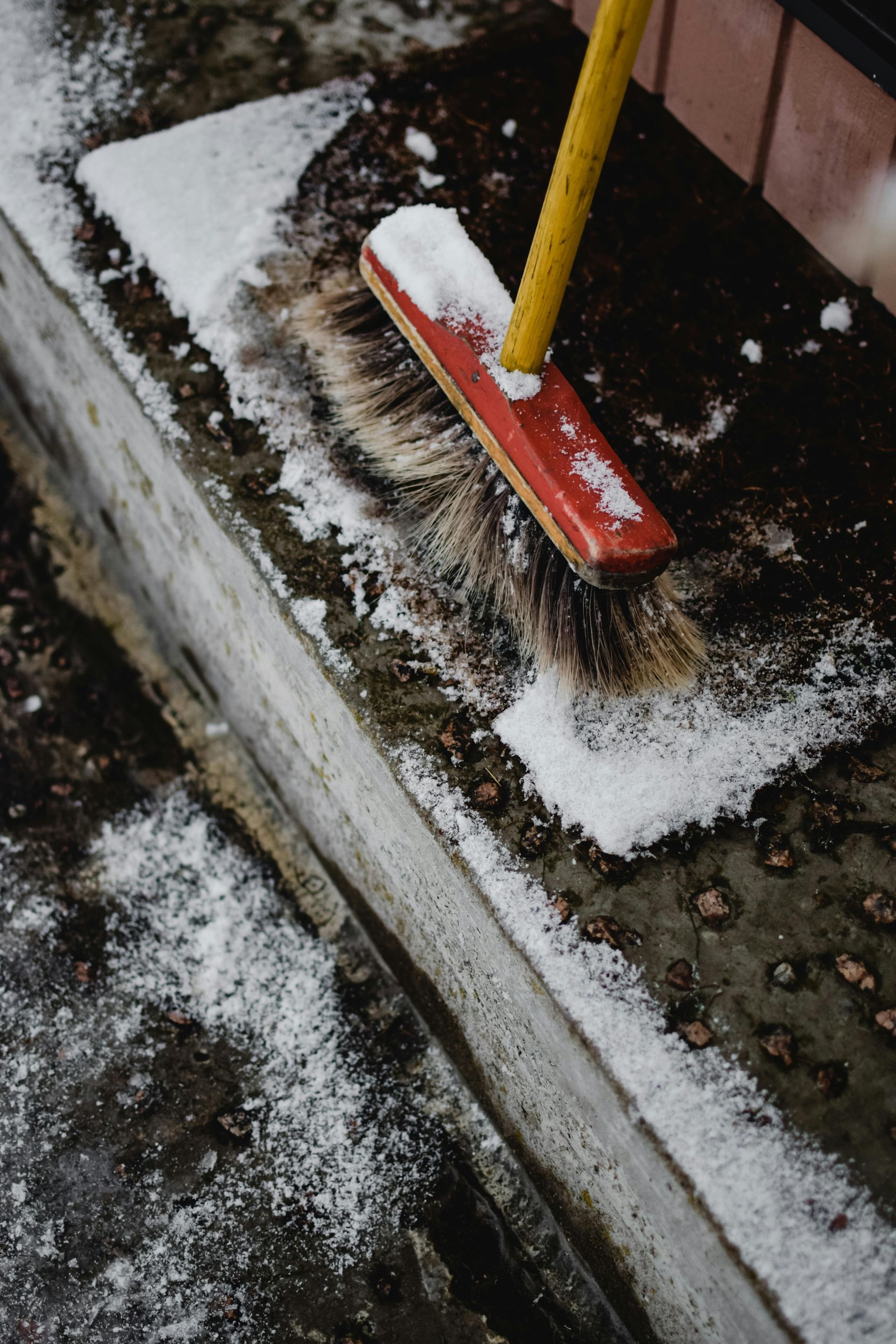A person sweeping salt from a concrete ledge with a red and yellow brush.