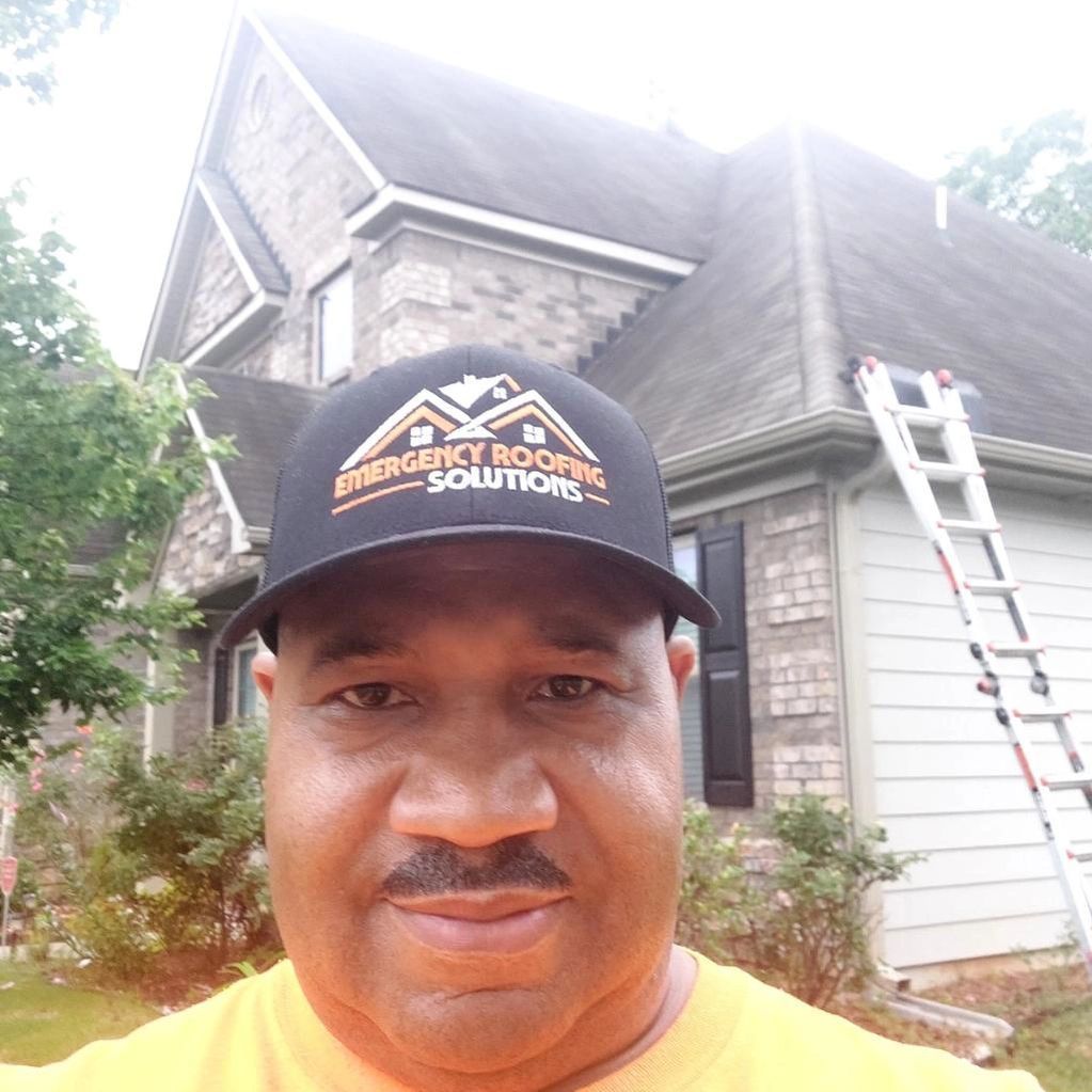 A man wearing a hat is standing in front of a house.