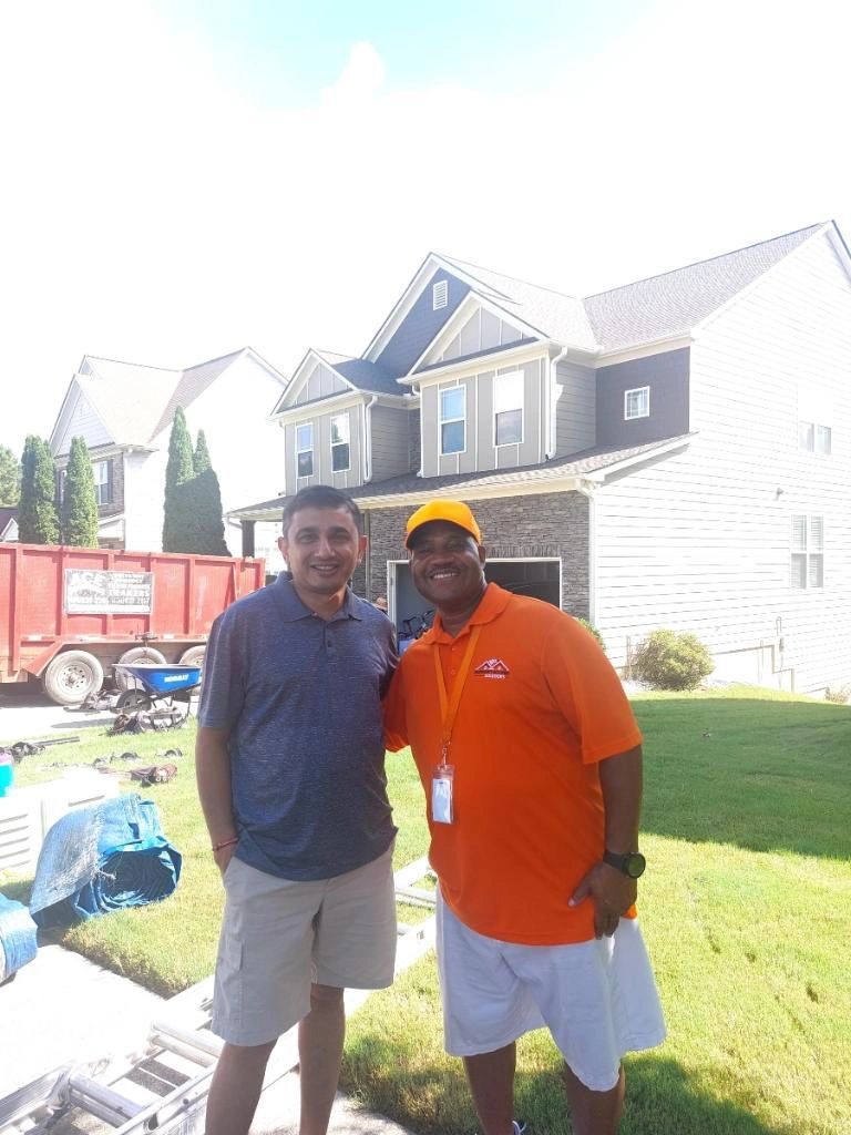 Two men are posing for a picture in front of a house.