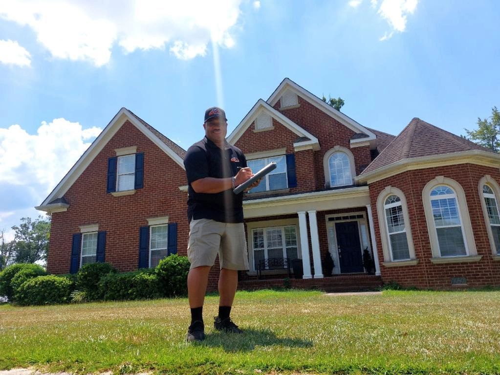 A man is standing in front of a large brick house holding a clipboard.
