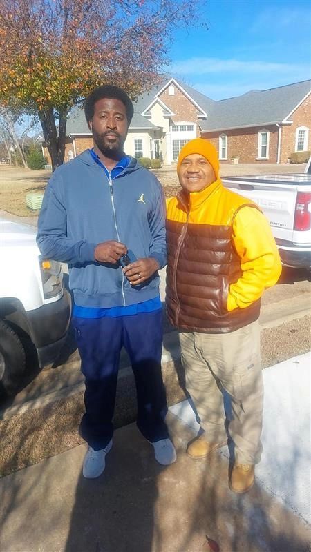Two men are standing next to each other on a sidewalk in front of a house.