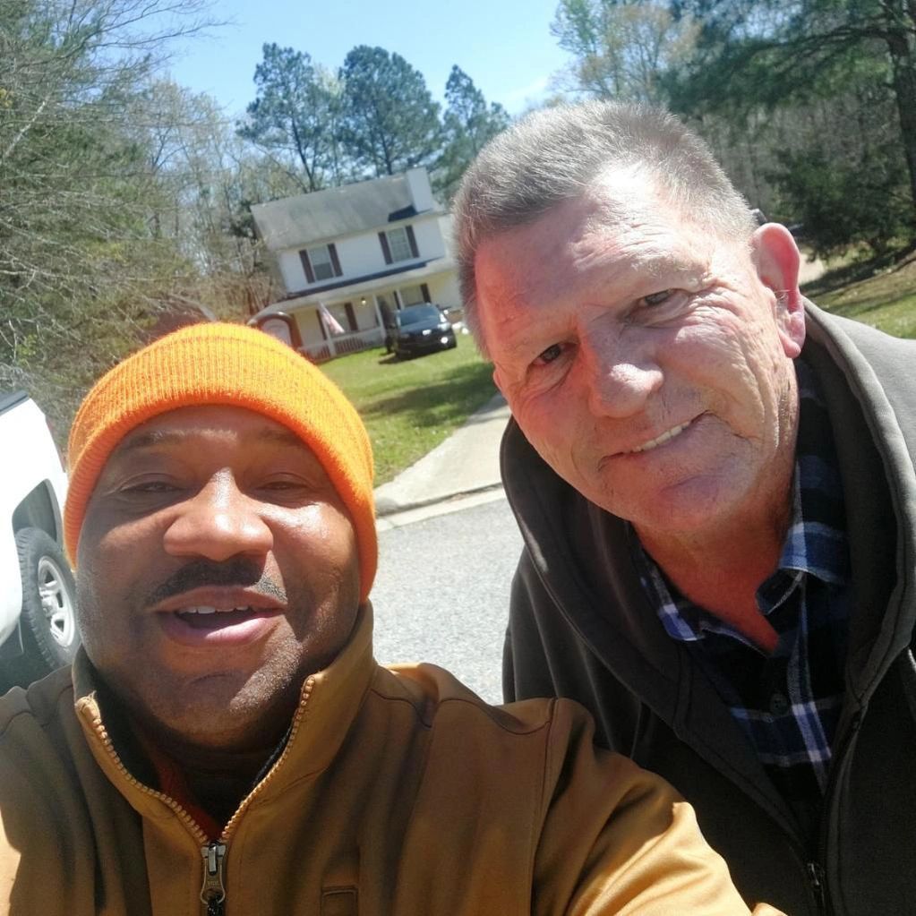 Two men are posing for a picture in front of a house