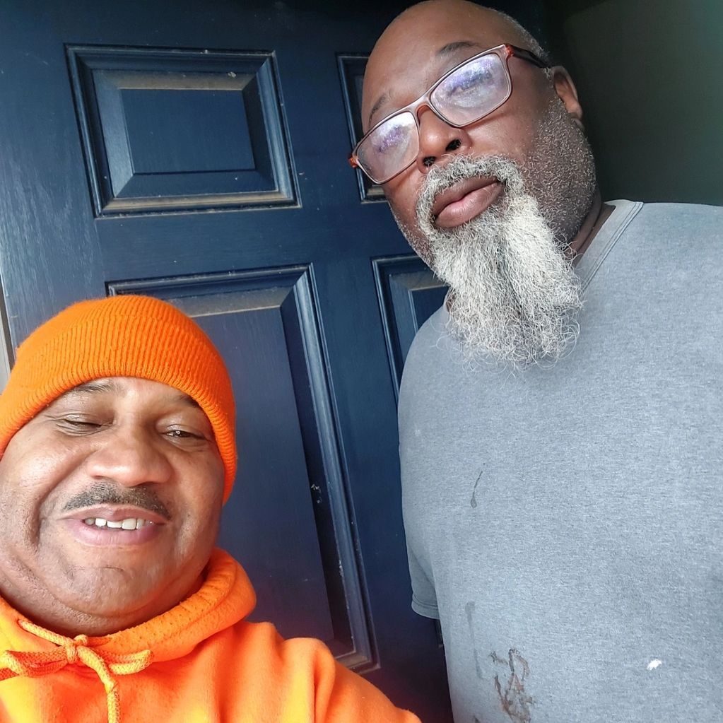 Two men with beards are posing for a picture in front of a blue door.