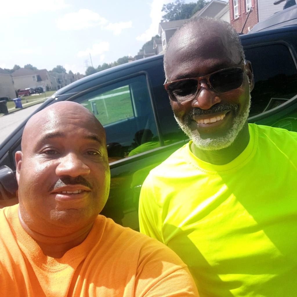 Two men are posing for a picture in front of a car