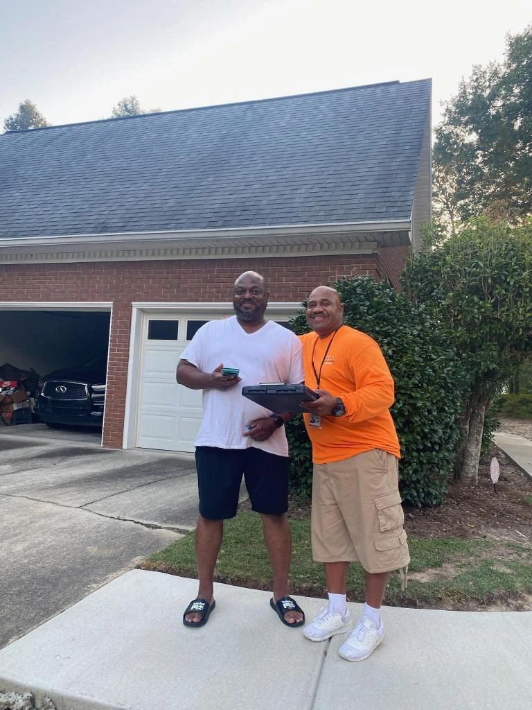 Two men are standing on a sidewalk in front of a garage.