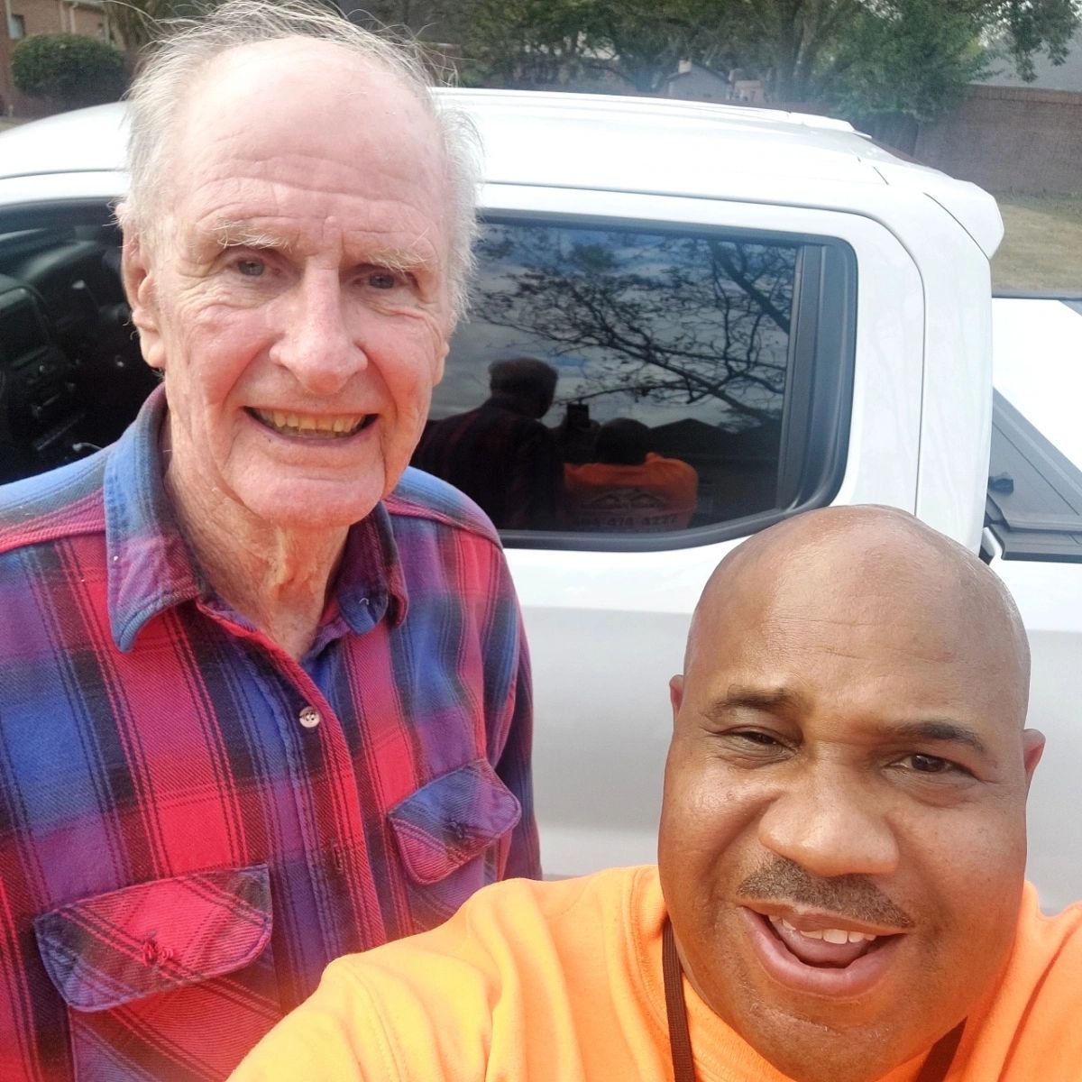 Two men are posing for a picture in front of a truck