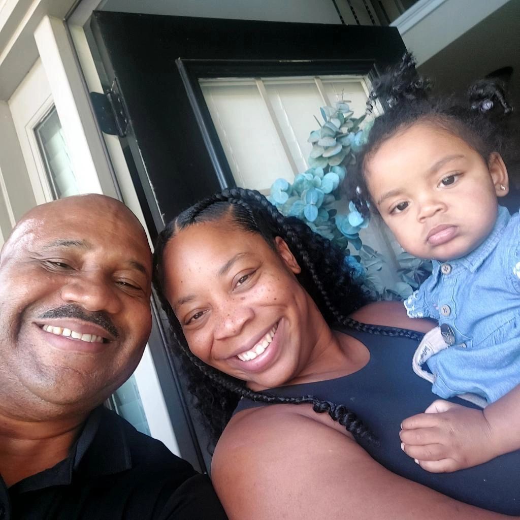 A man and a woman are holding a baby and smiling for the camera.