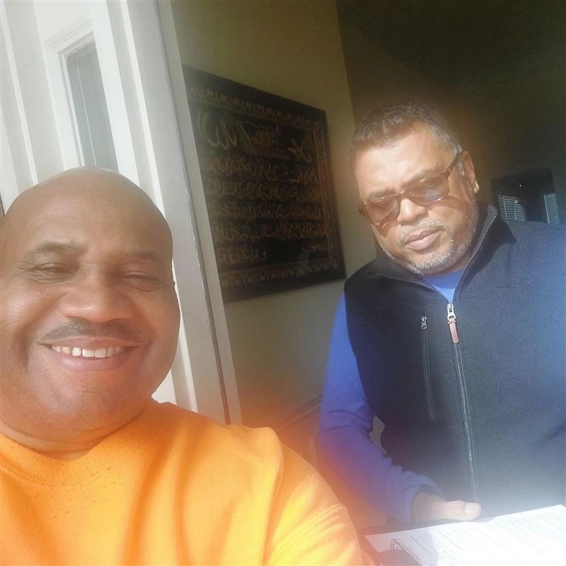 Two men are posing for a picture and one is wearing an orange shirt