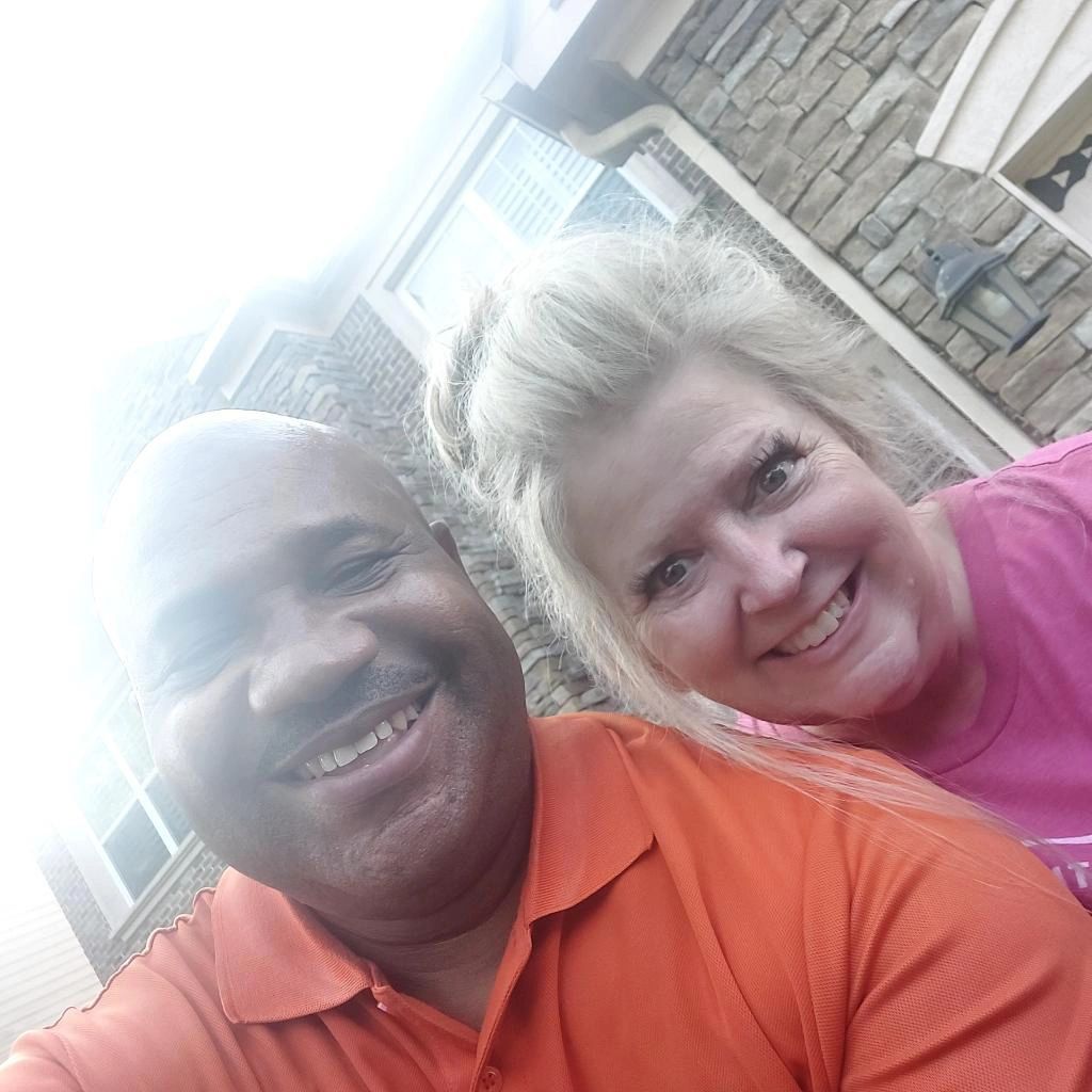 A man and a woman are smiling for a selfie in front of a stone building.
