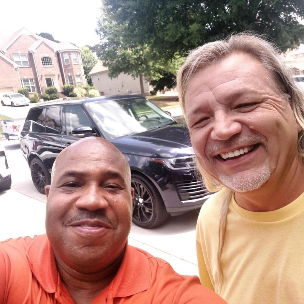 Two men are posing for a picture in front of a car