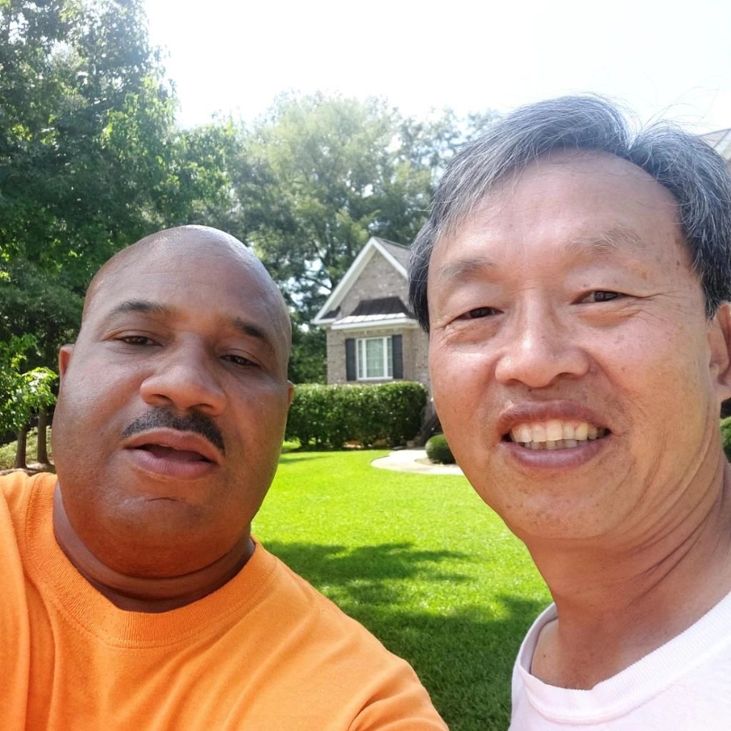 Two men are posing for a picture in front of a house.