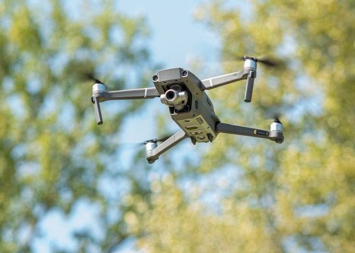 A drone is flying in the sky above trees.