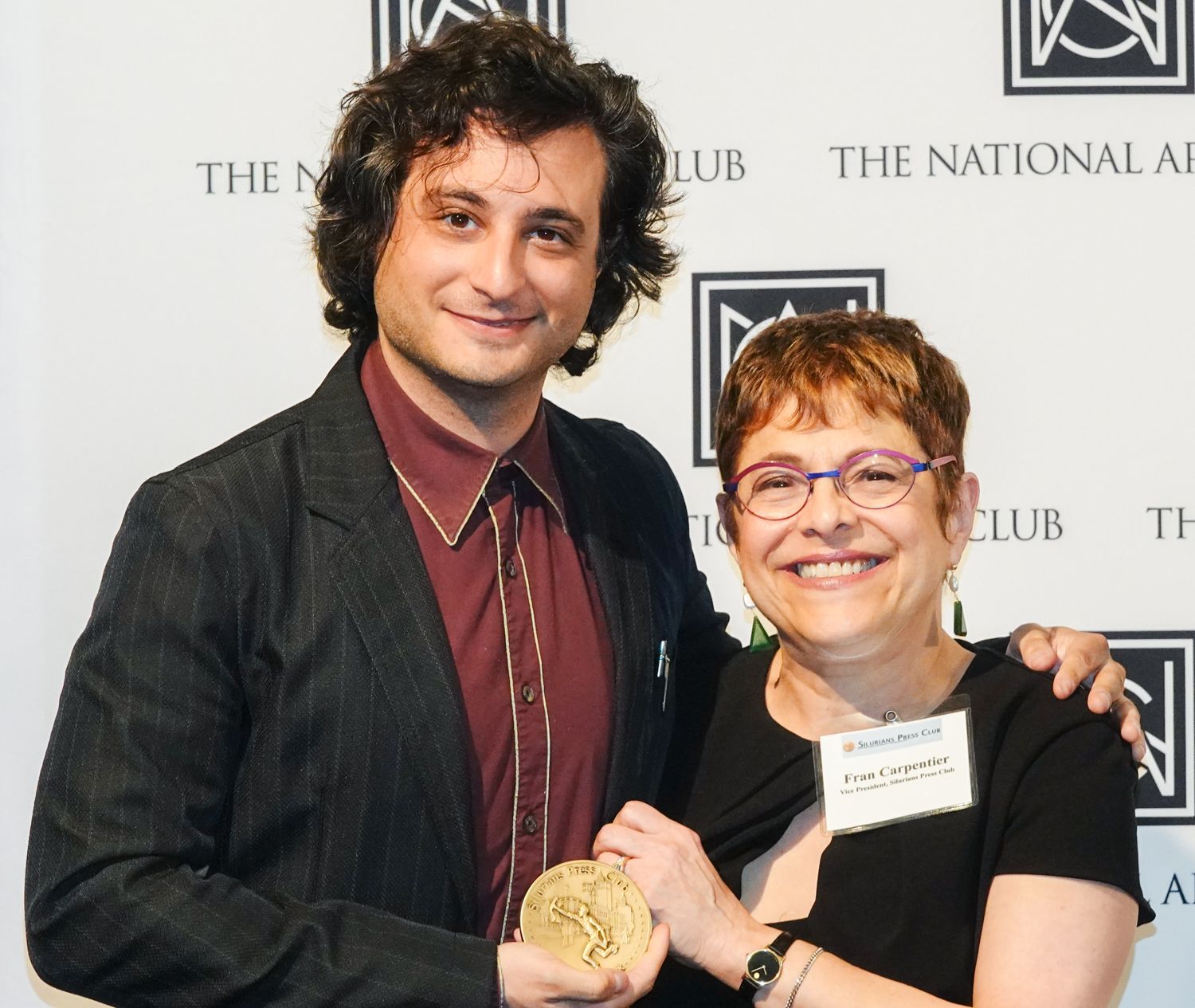 A man and woman are posing for a picture in front of a wall that says the national club