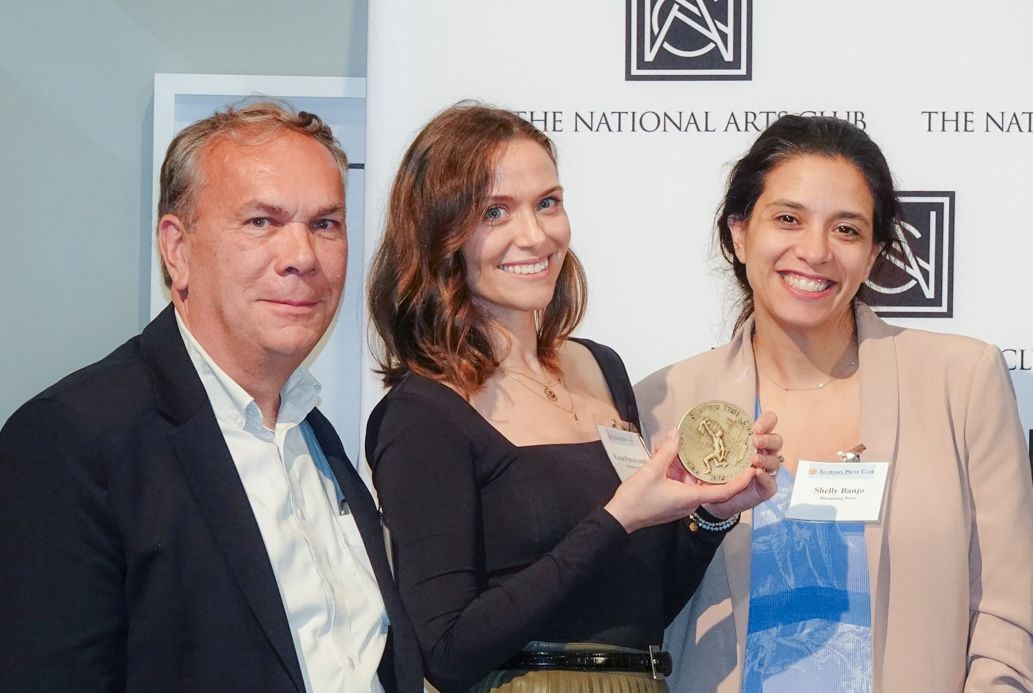 A man and two women are standing next to each other holding a medal.