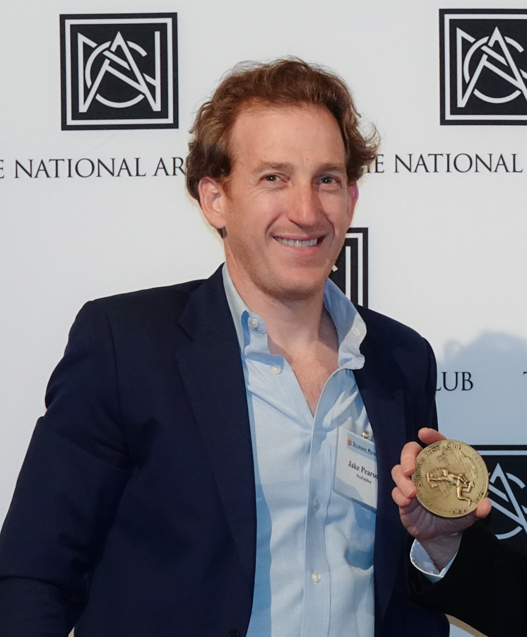 A man in a suit is holding a medal in front of a wall that says national