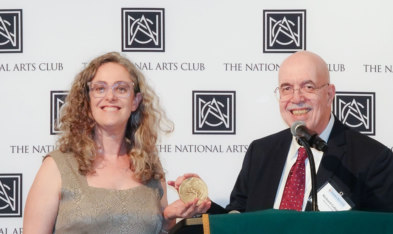 A man and a woman are standing in front of a wall that says national arts club