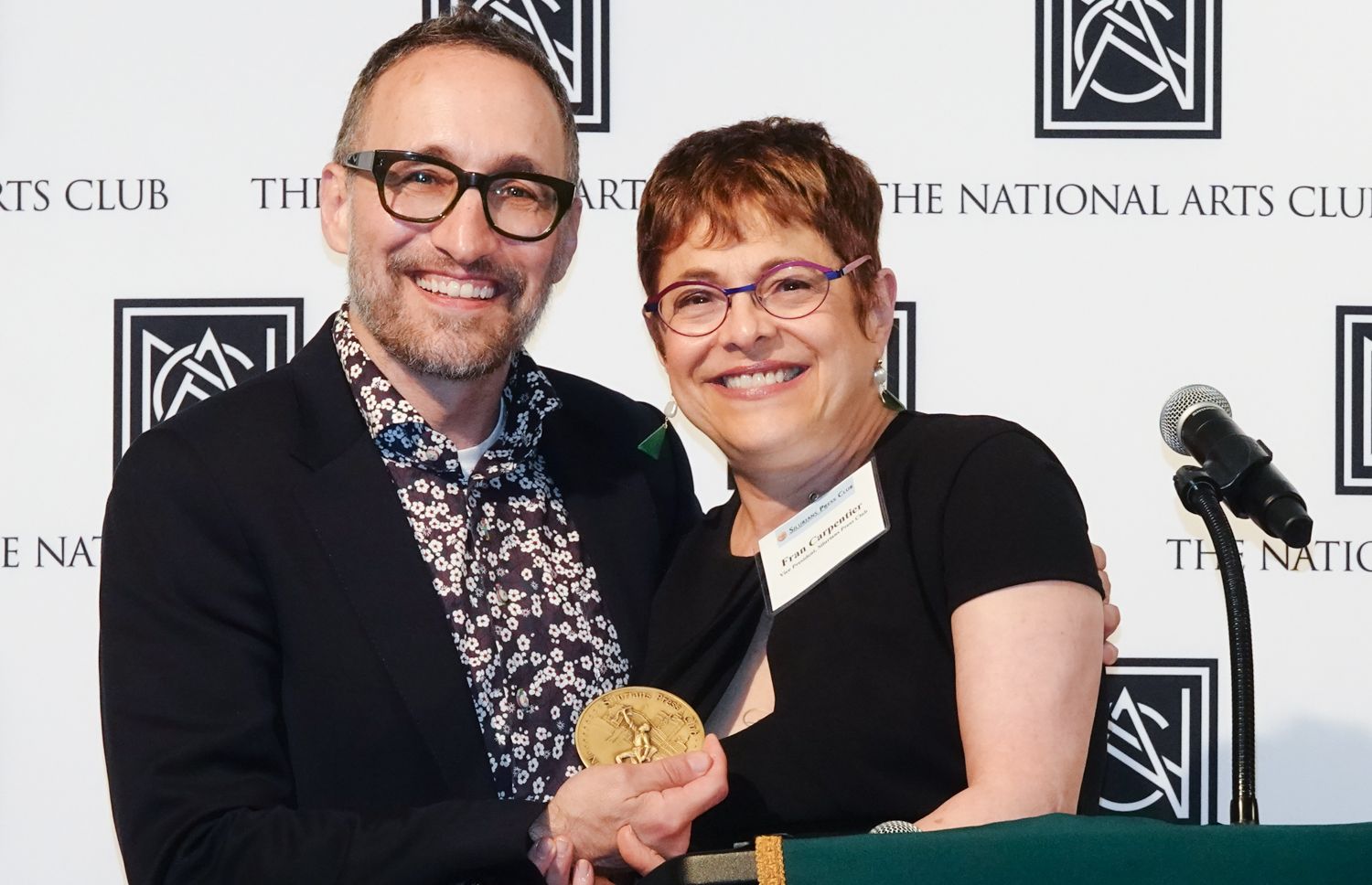 A man and a woman are standing next to each other holding a gold medal.