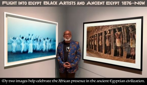 A man is standing in front of two framed pictures on a wall.