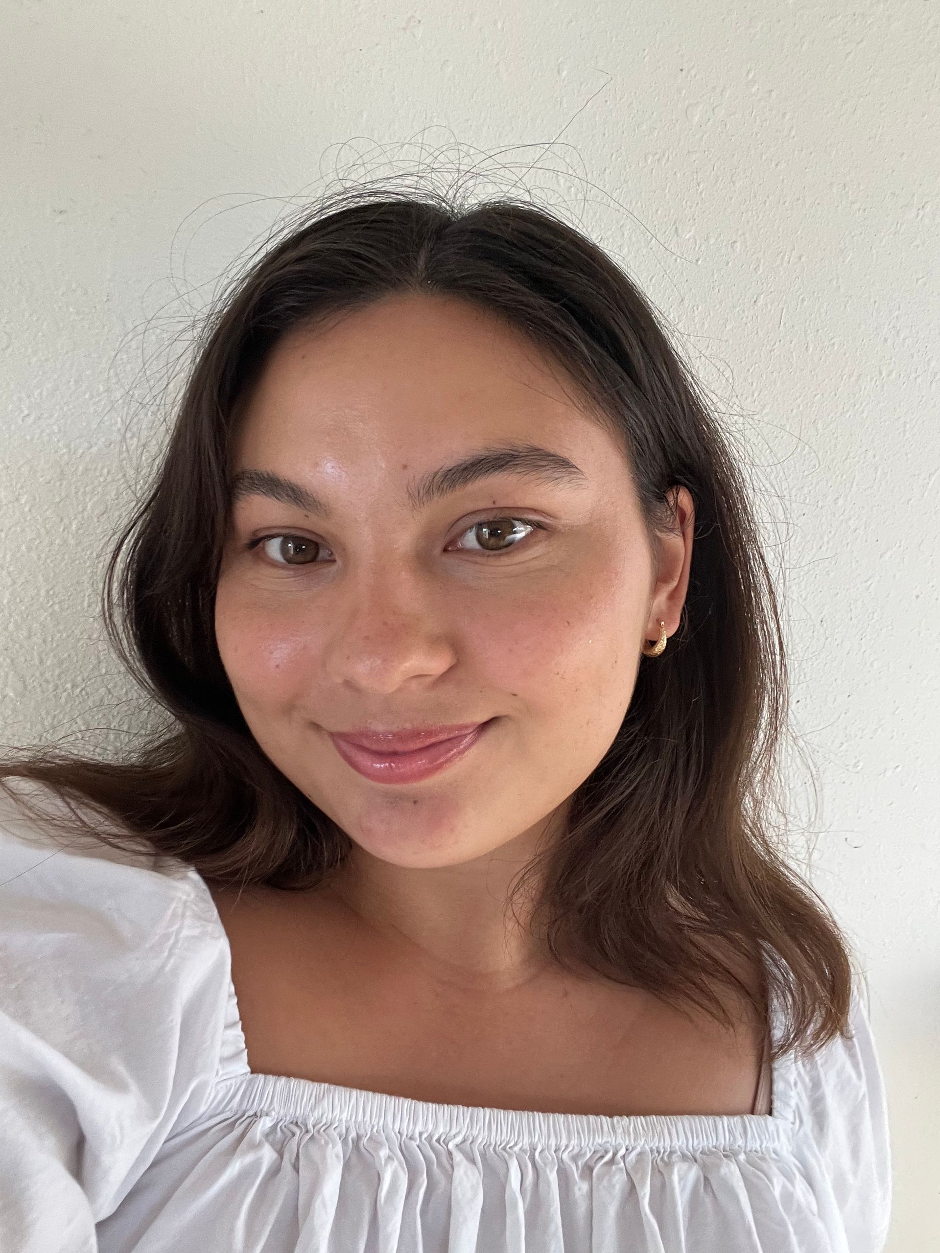 Smiling woman in a white off-shoulder blouse against a plain light background