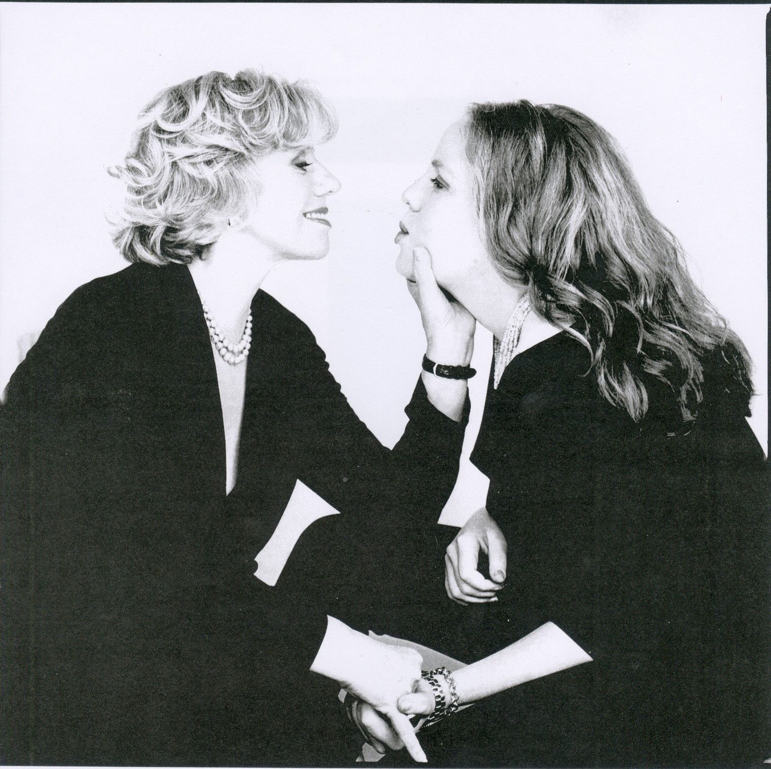 Two women, one touching the other's face, smiling. Black and white photo.