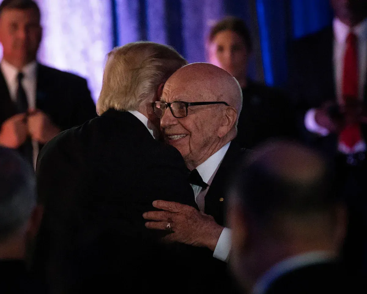 Donald Trump and Rupert Murdoch embrace warmly at an event. Murdoch smiles, wearing glasses; Trump's face is partially obscured.