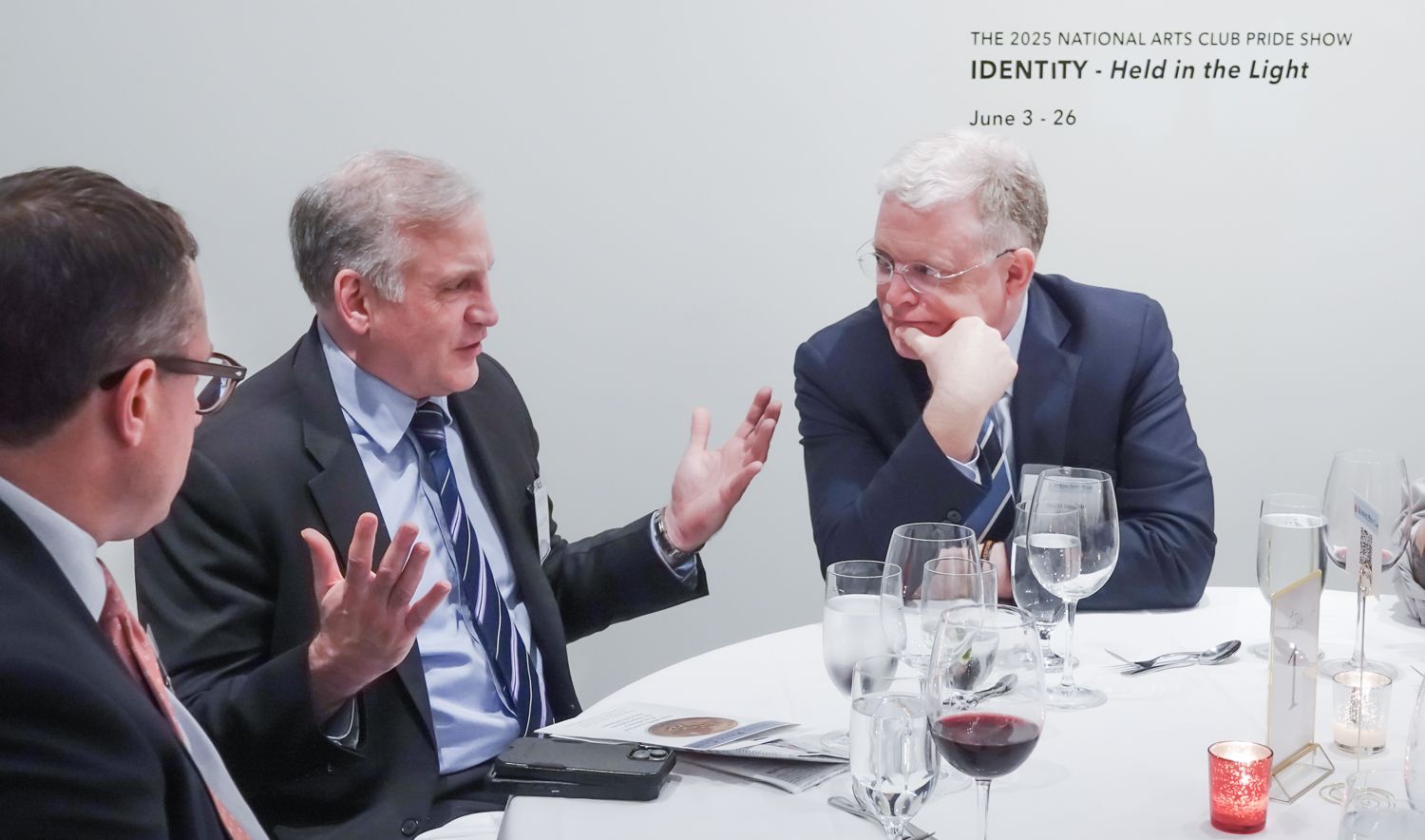 Three men are sitting at a table with wine glasses and a candle.