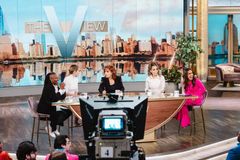Talk show panel in a studio with host desk, camera, and city skyline backdrop