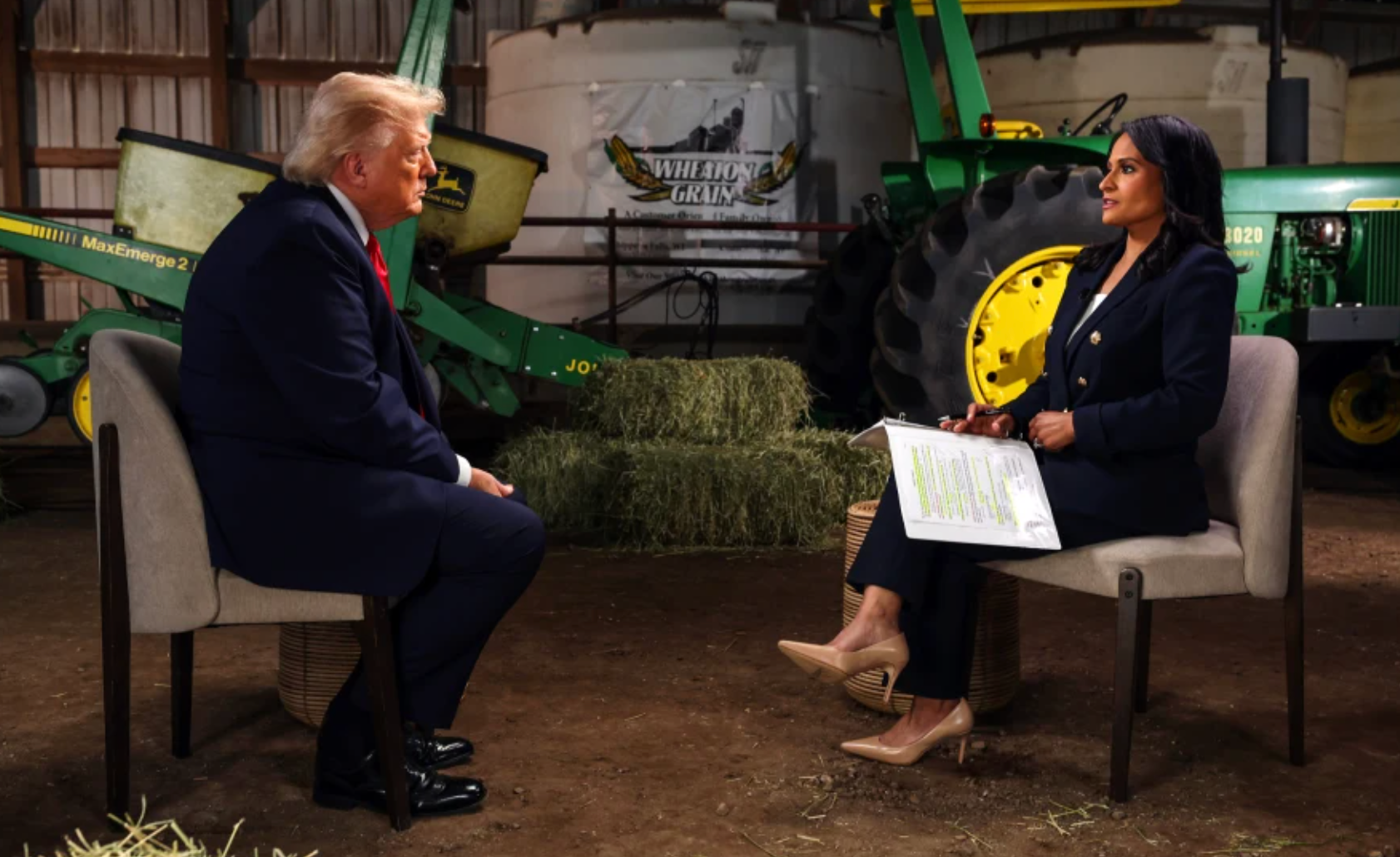 Two people seated in a barn-like setting, holding an interview beside a green tractor.