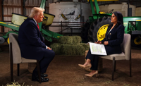 Two people seated in a barn-like setting, holding an interview beside a green tractor.