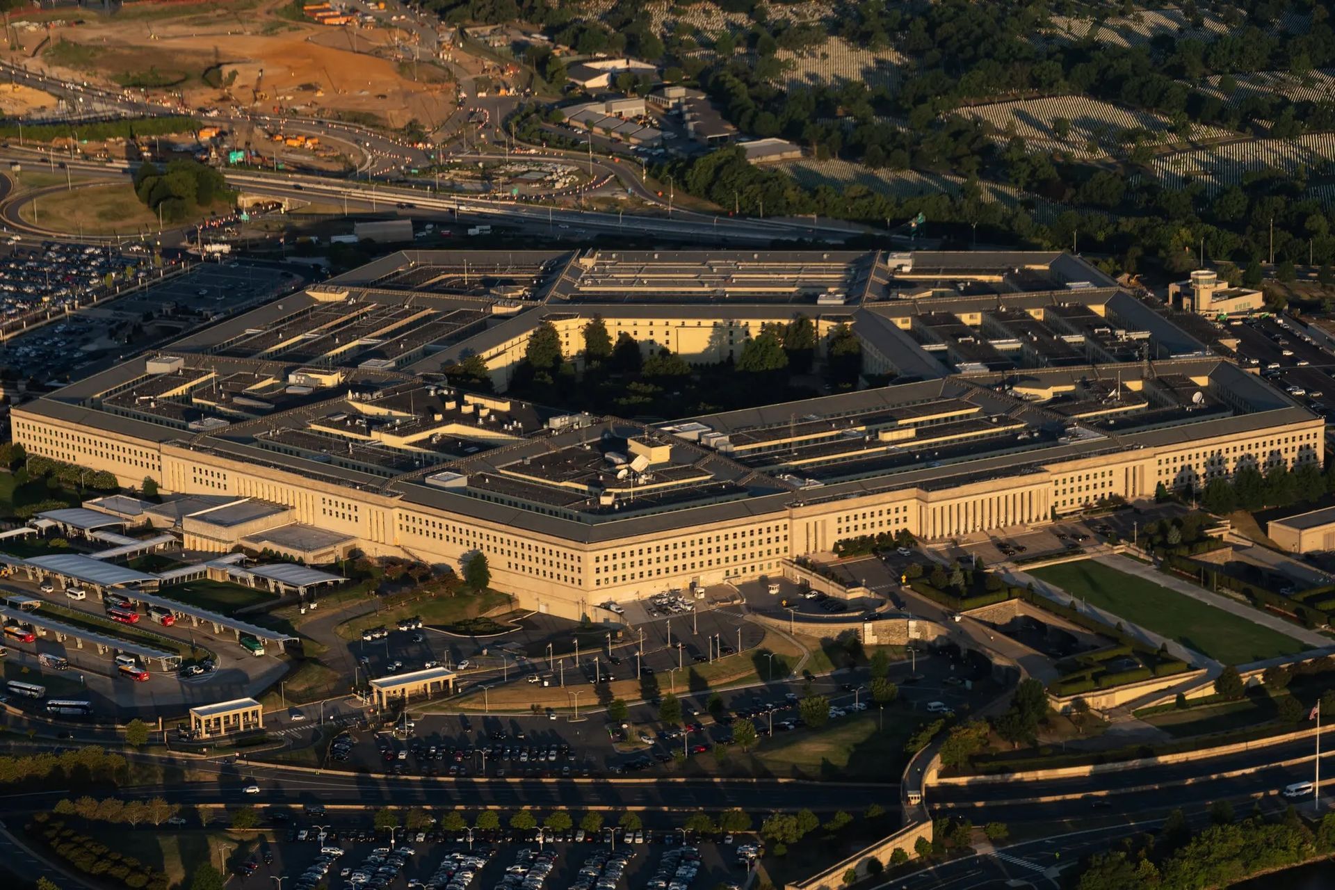 Aerial view of the Pentagon building, a five-sided structure, surrounded by parking lots and roads, under a sunny sky.