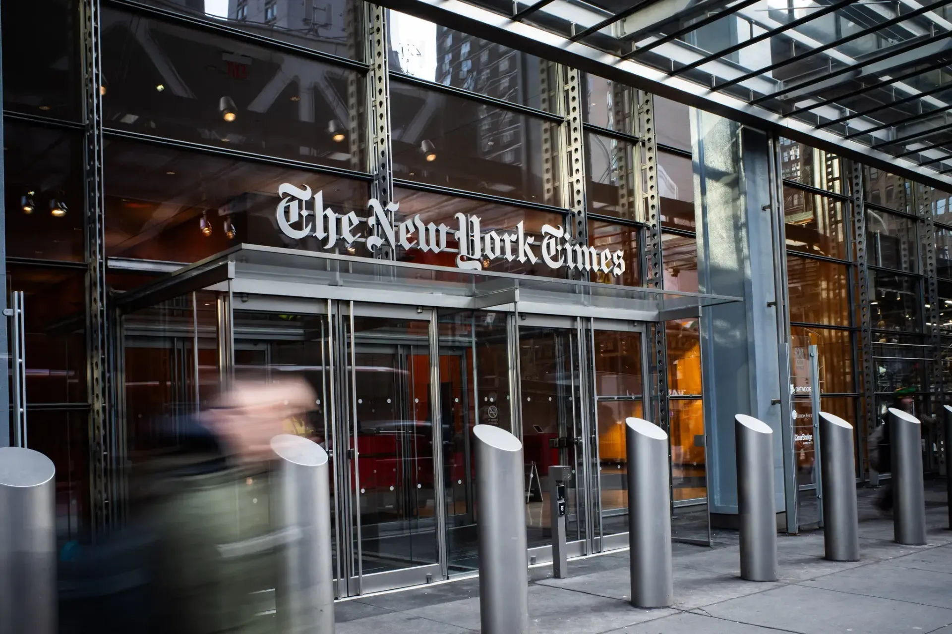 The New York Times building entrance with a blurred person walking past.