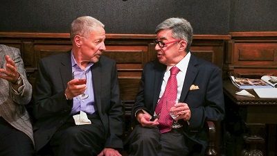 Two men in suits and ties are sitting in chairs talking to each other.