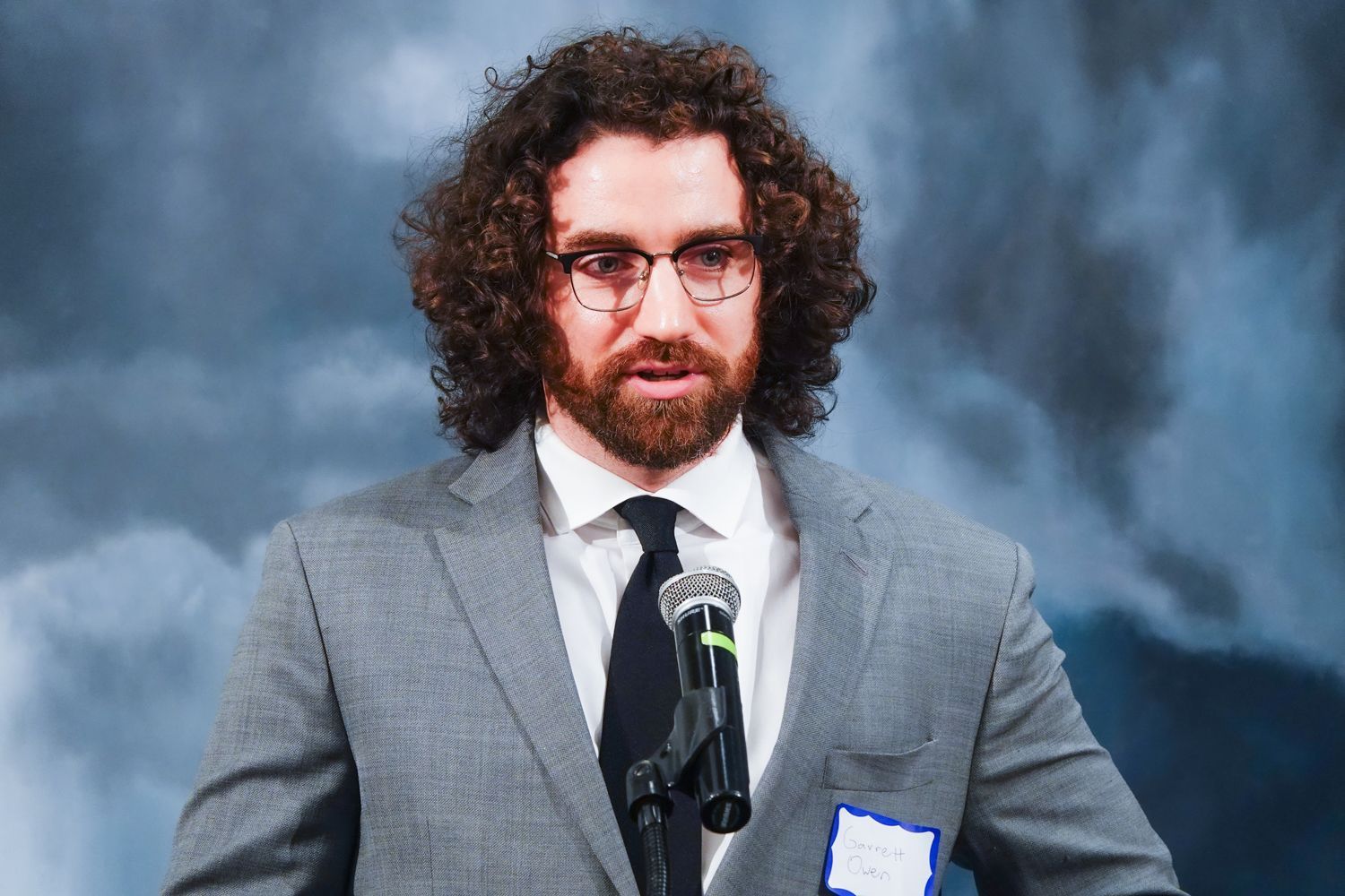 A man in a suit and tie is standing in front of a microphone.