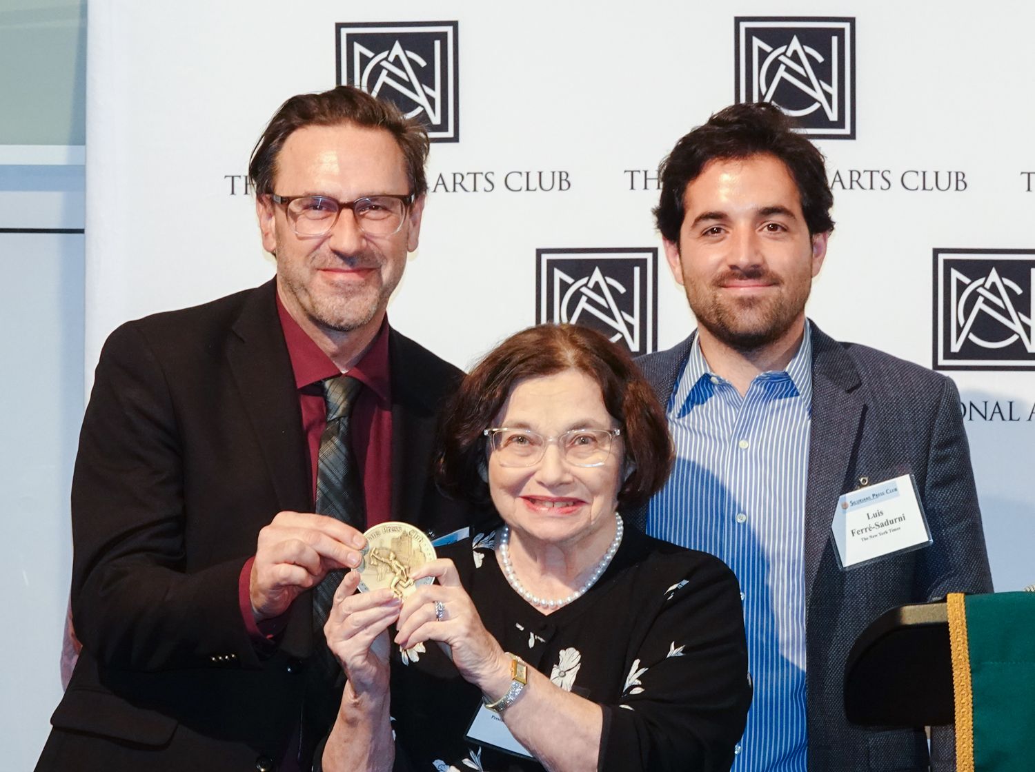 Three people are posing for a picture in front of a wall that says arts club