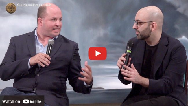 Two men are sitting next to each other talking into microphones.