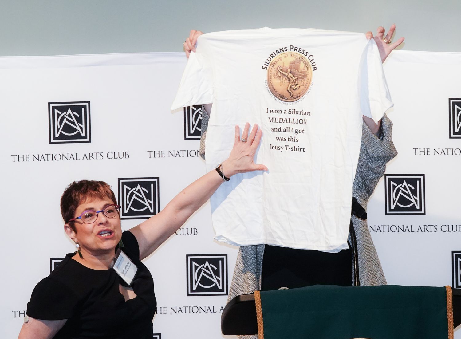 A woman is holding up a white t-shirt that says the national arts club
