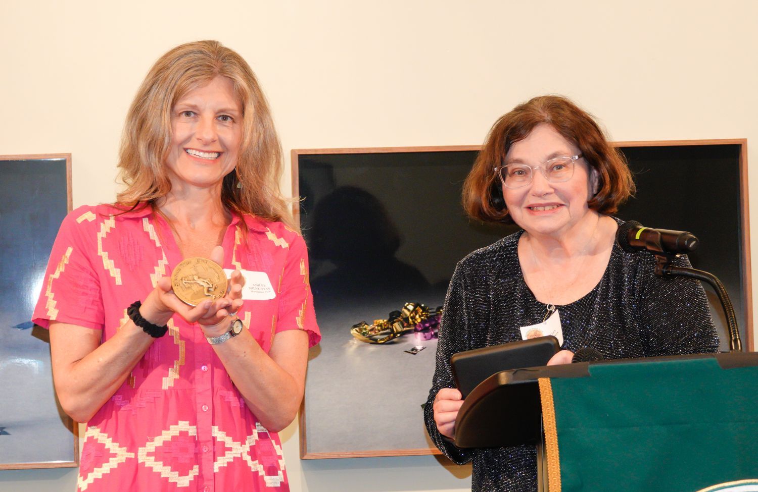 Two women are standing next to each other and one is holding a trophy