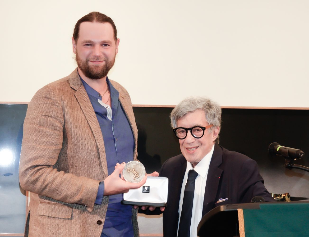 A man in a suit is giving a medal to another man
