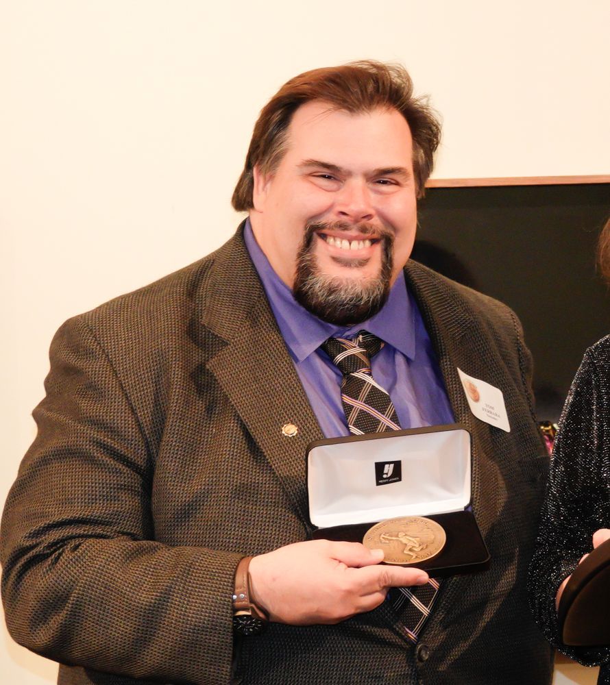 A man in a suit and tie is holding a medal with the letter p on it