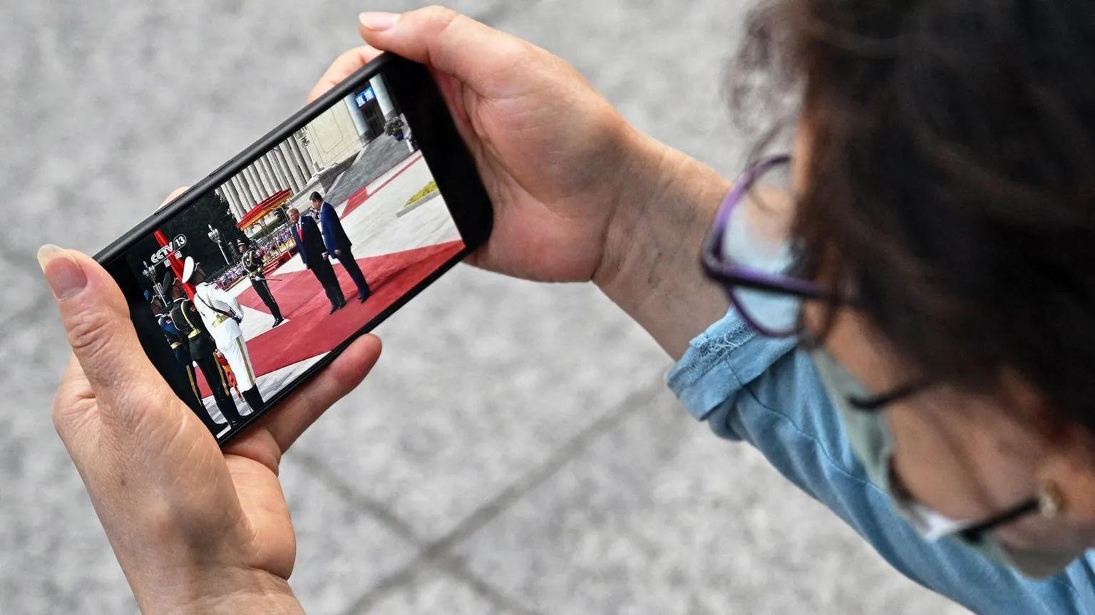 Person holding a smartphone horizontally, watching a formal event on the screen.
