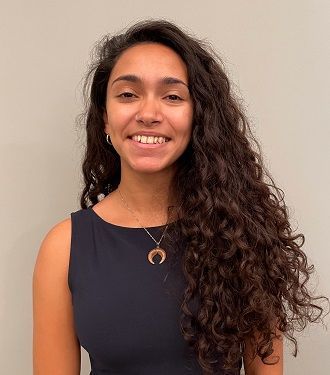 A woman with long curly hair is smiling and wearing a necklace.