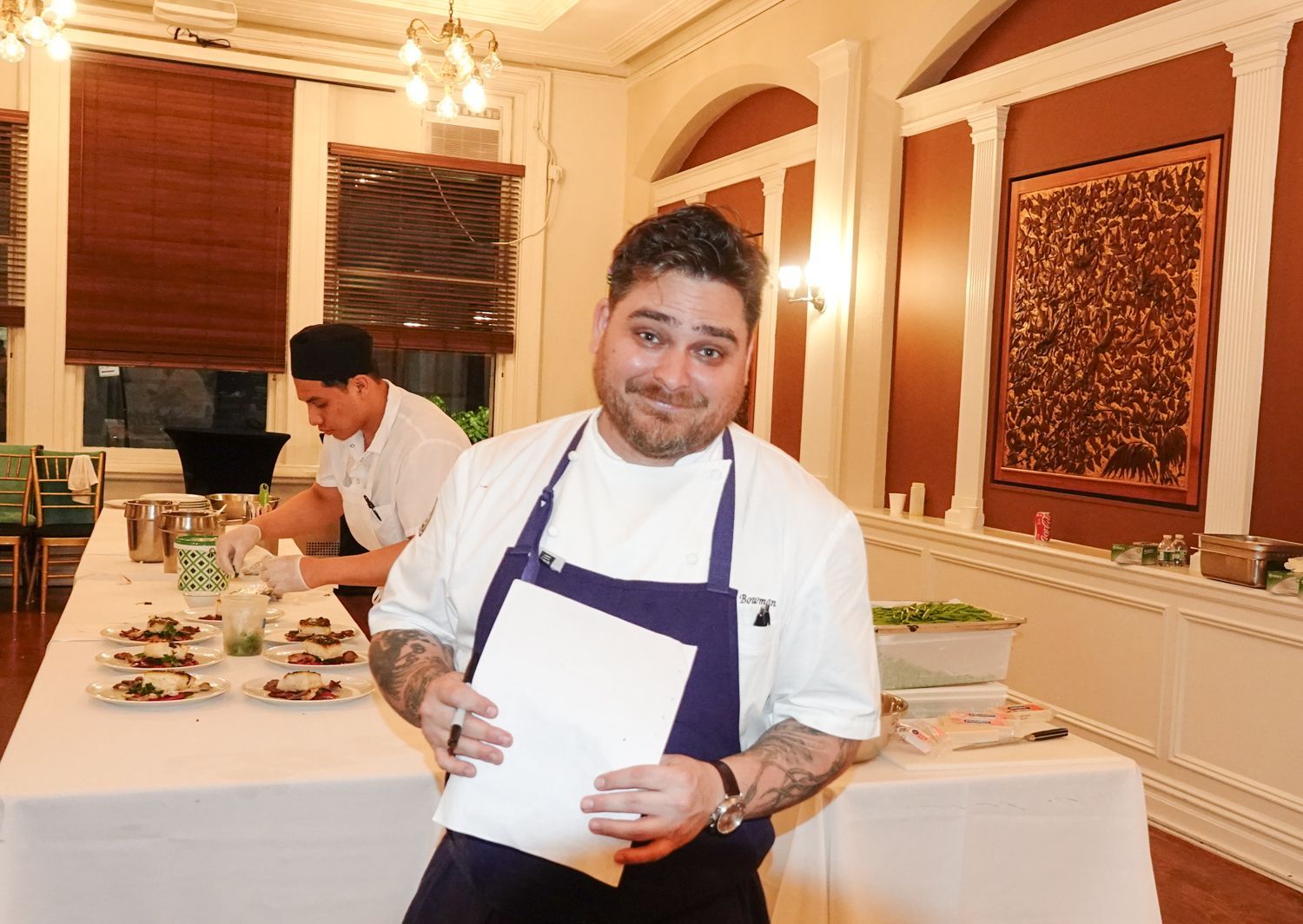 A man in an apron is holding a piece of paper in a kitchen.
