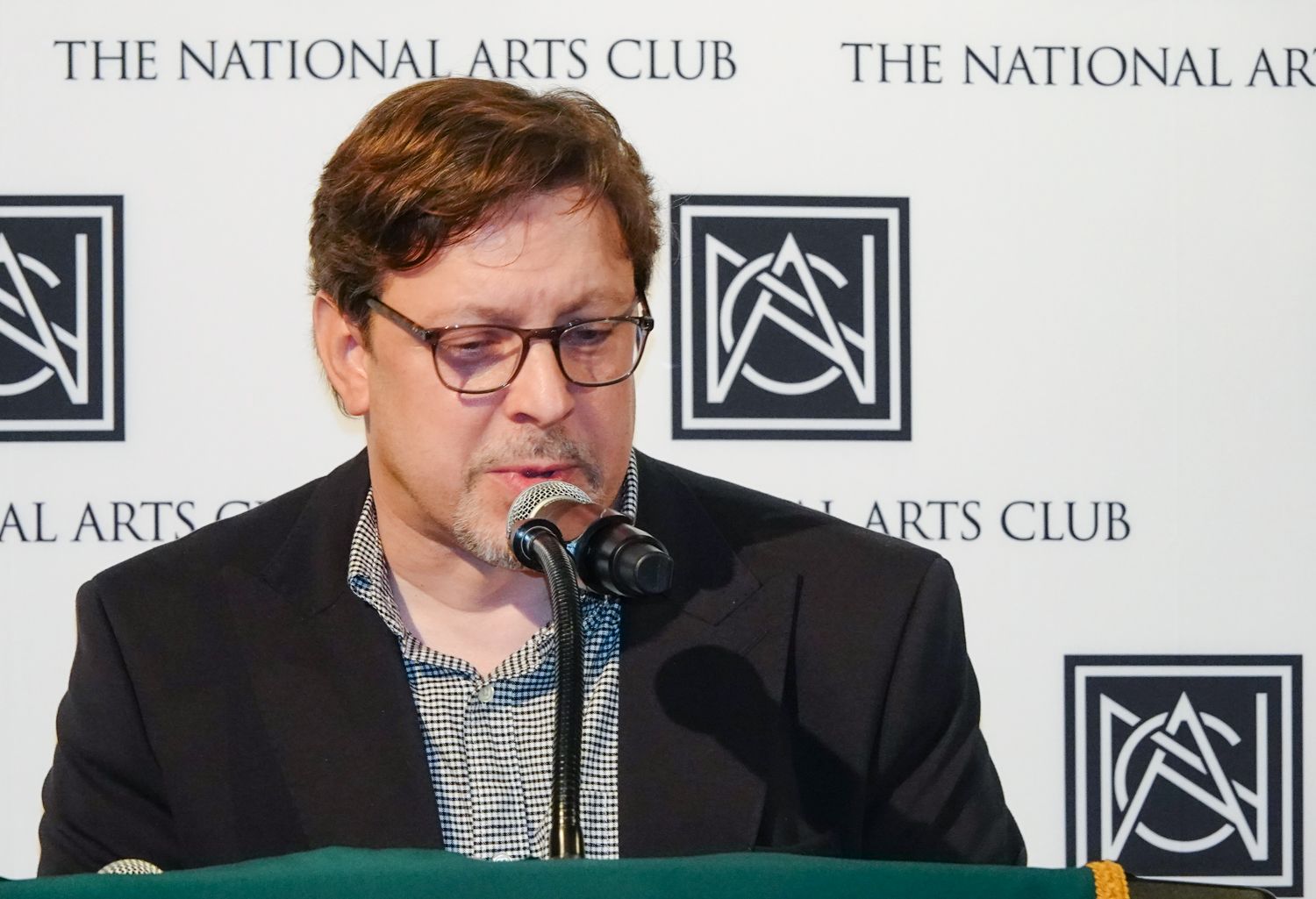 A man is speaking into a microphone at the national arts club